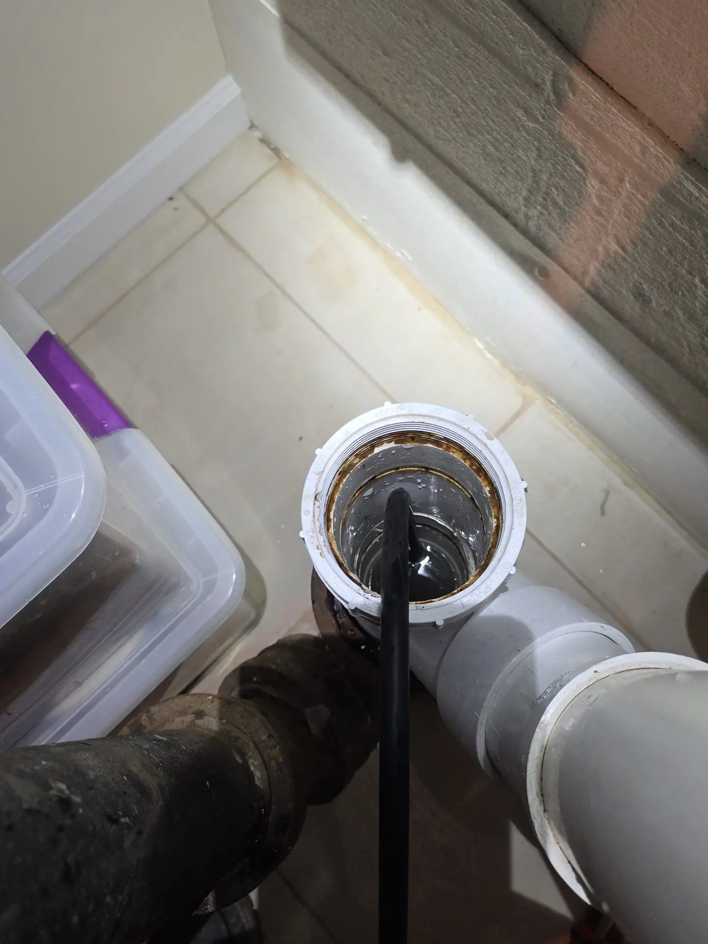 Plumber feeding a drain cleaning cable auger into a PVC pipe cleanout to clear a clog