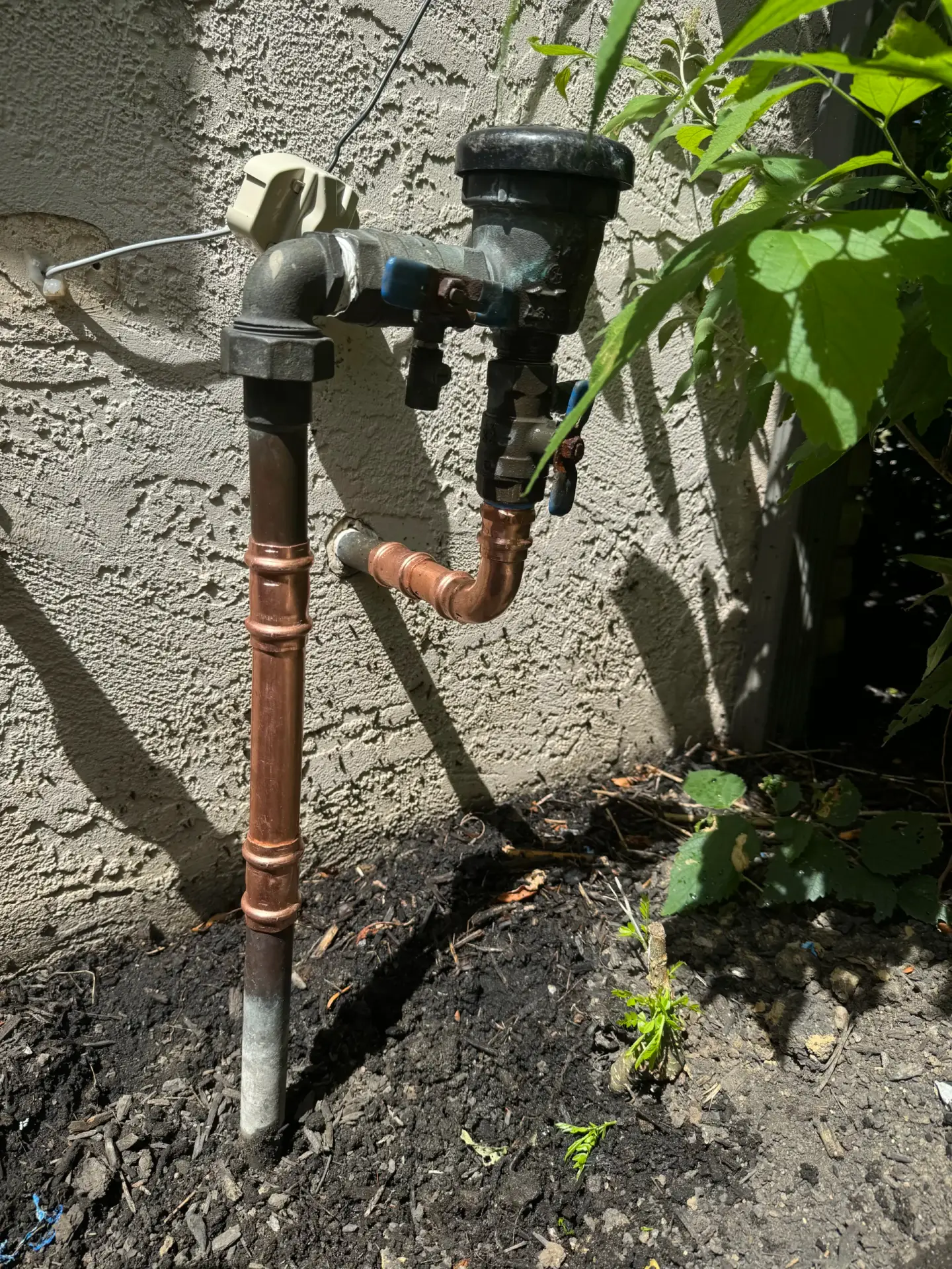 Exterior hose bib and backflow preventer mounted on a stucco wall